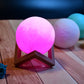 Moon lamp in pink with wooden stand, suitable for bedroom decor.